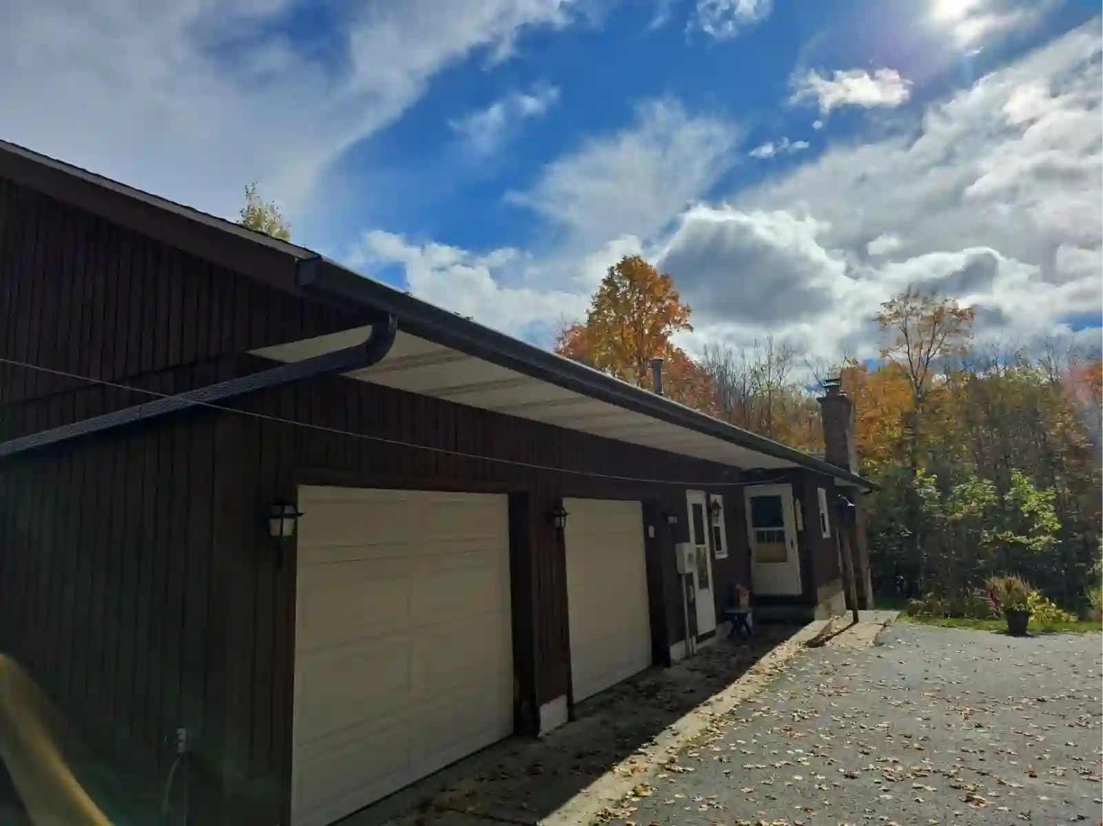 Brown roofline with new gutters against fall color and blue sky
