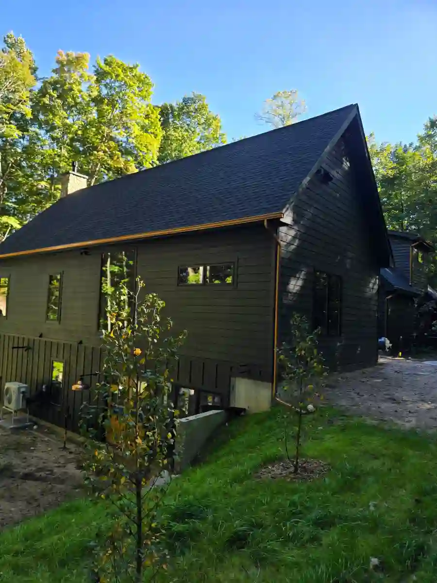 Dark green Northern Michigan home with new black seamless gutters and downspouts, surrounded by trees